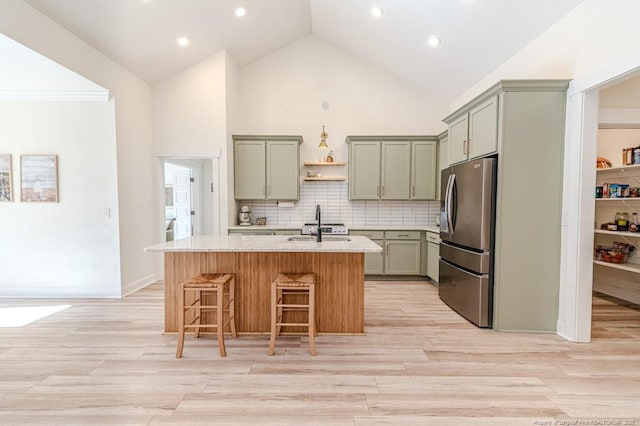 kitchen featuring light stone countertops, a center island with sink, stainless steel fridge, a kitchen bar, and high vaulted ceiling