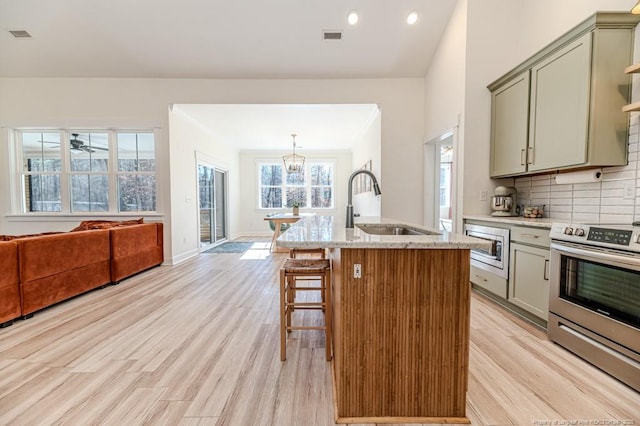 kitchen with a kitchen island with sink, appliances with stainless steel finishes, light hardwood / wood-style floors, decorative backsplash, and sink