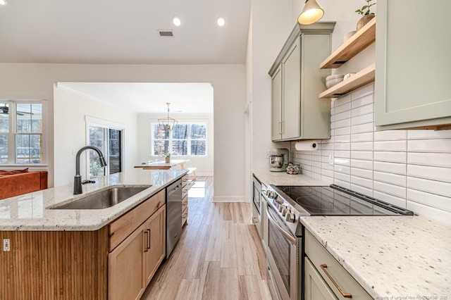 kitchen featuring appliances with stainless steel finishes, an island with sink, light stone countertops, sink, and decorative light fixtures