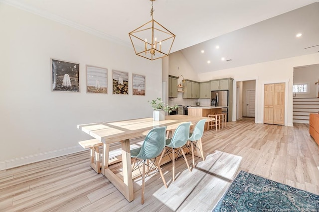 dining area with high vaulted ceiling, a notable chandelier, and light hardwood / wood-style flooring