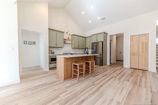 kitchen with a kitchen island with sink, stainless steel fridge, a kitchen bar, high vaulted ceiling, and tasteful backsplash