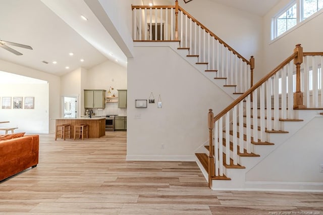 stairs featuring sink, ceiling fan, a towering ceiling, and wood-type flooring