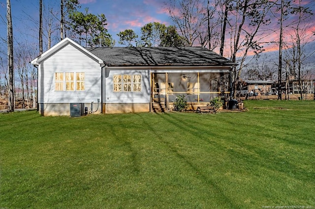 back house at dusk with a lawn, central AC, and a sunroom