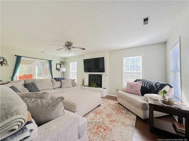 living room featuring ceiling fan, dark wood-type flooring, a healthy amount of sunlight, and a textured ceiling