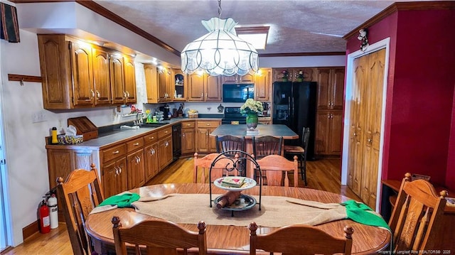 kitchen with pendant lighting, sink, crown molding, black appliances, and light wood-type flooring