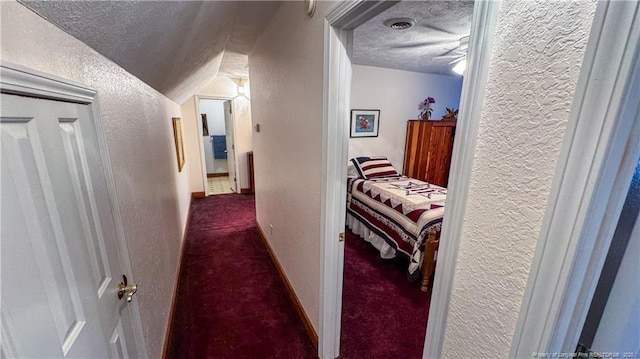 corridor with lofted ceiling, a textured ceiling, and dark colored carpet