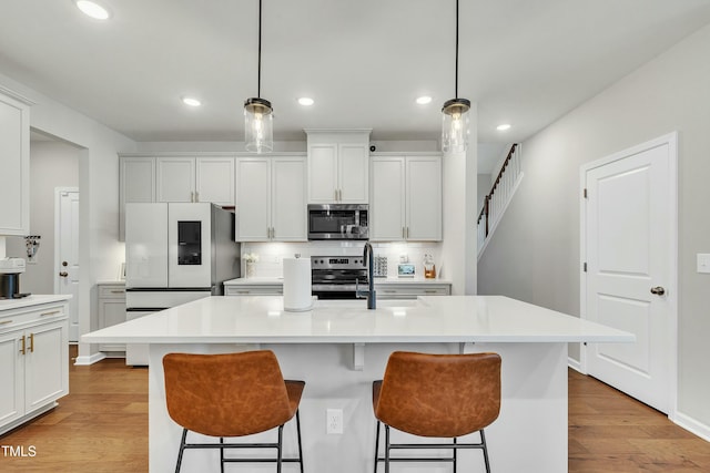 kitchen with white cabinets, hanging light fixtures, appliances with stainless steel finishes, and an island with sink