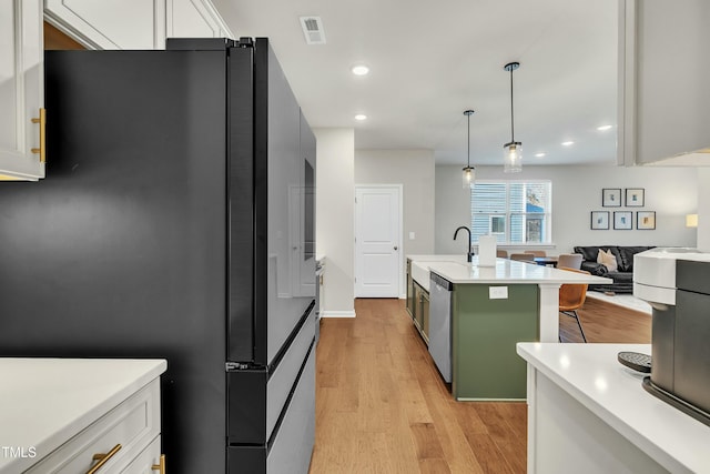 kitchen with white cabinetry, an island with sink, black fridge, dishwasher, and hanging light fixtures