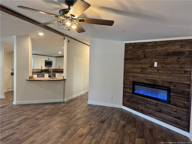 unfurnished living room with a large fireplace, ceiling fan, crown molding, and dark hardwood / wood-style floors