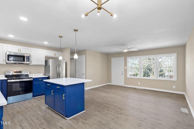 kitchen featuring pendant lighting, appliances with stainless steel finishes, blue cabinets, and white cabinets