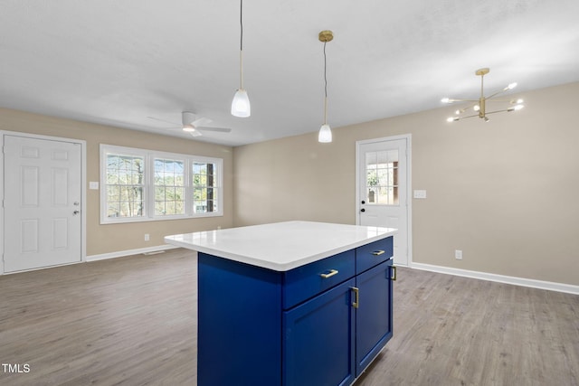 kitchen with ceiling fan with notable chandelier, pendant lighting, blue cabinets, a center island, and light hardwood / wood-style flooring