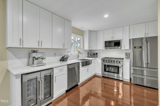 kitchen with white cabinetry, premium appliances, tasteful backsplash, beverage cooler, and sink