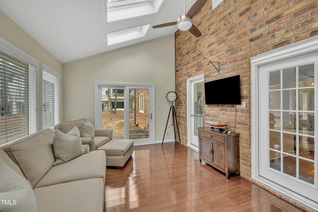 living room with light wood-type flooring, ceiling fan, a skylight, and high vaulted ceiling