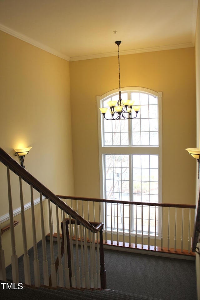 staircase featuring a healthy amount of sunlight, crown molding, and an inviting chandelier