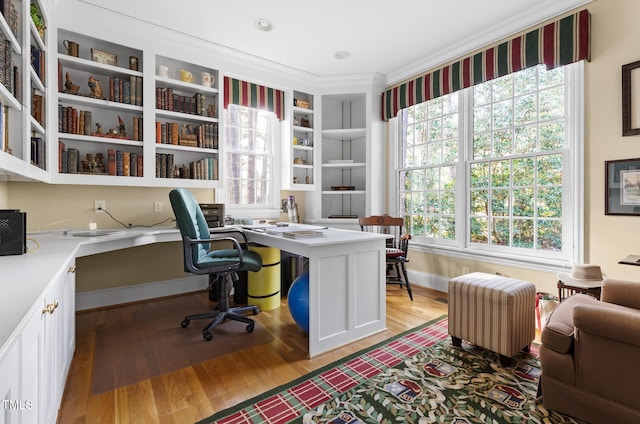 office space featuring built in desk, light wood-type flooring, crown molding, and built in features