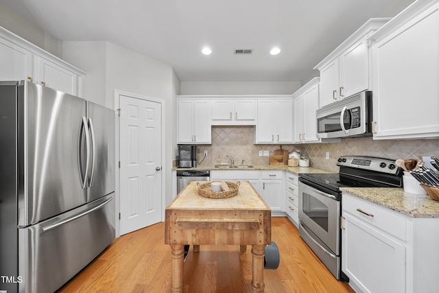 kitchen featuring stainless steel appliances, backsplash, light stone countertops, white cabinets, and sink