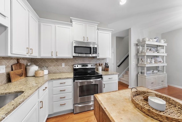 kitchen featuring white cabinets, stainless steel appliances, decorative backsplash, light stone counters, and light hardwood / wood-style flooring