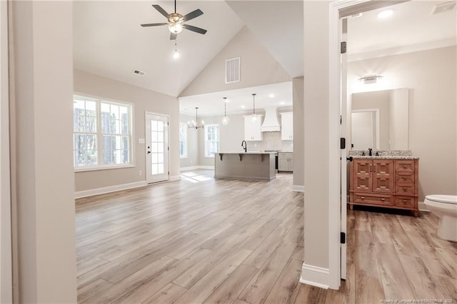 living room with light wood-type flooring, sink, ceiling fan with notable chandelier, and high vaulted ceiling