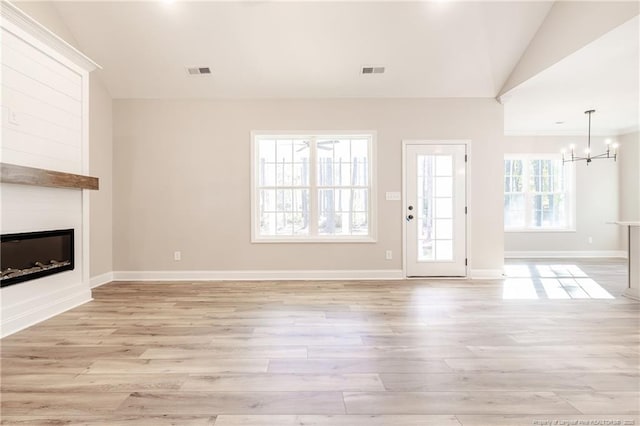 unfurnished living room featuring light wood-type flooring, an inviting chandelier, and lofted ceiling