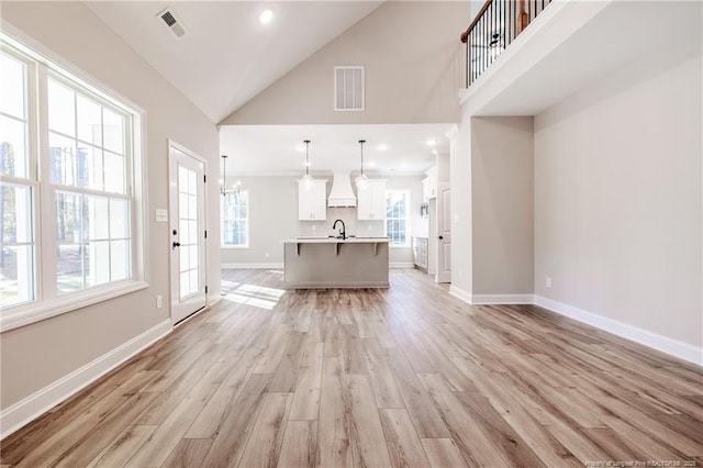 unfurnished living room featuring high vaulted ceiling, sink, and light hardwood / wood-style flooring