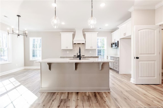 kitchen featuring custom exhaust hood, an island with sink, and white cabinetry