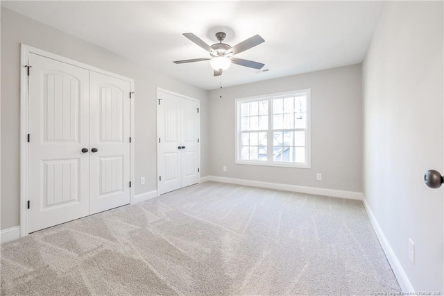 unfurnished bedroom with light carpet, ceiling fan, and two closets