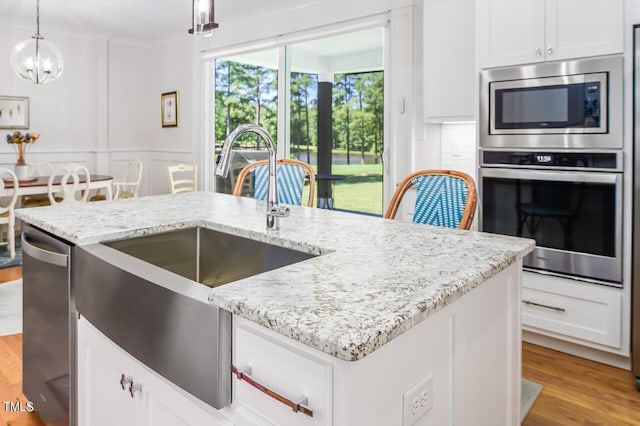 kitchen featuring light stone counters, decorative light fixtures, light hardwood / wood-style floors, stainless steel appliances, and a kitchen island with sink