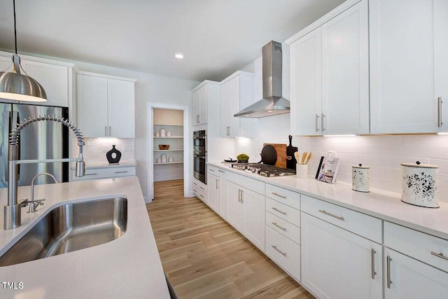 kitchen with pendant lighting, appliances with stainless steel finishes, wall chimney exhaust hood, decorative backsplash, and sink