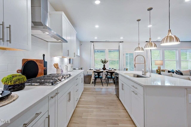 kitchen featuring wall chimney range hood, a center island with sink, decorative backsplash, sink, and white cabinets