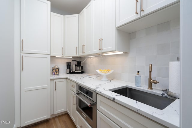 kitchen with light stone countertops, white cabinets, tasteful backsplash, sink, and oven