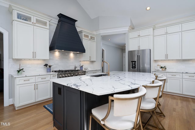 kitchen featuring vaulted ceiling, high quality fridge, a kitchen island with sink, custom range hood, and white cabinets