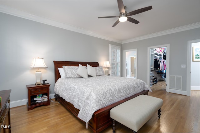 bedroom with a spacious closet, connected bathroom, a closet, ornamental molding, and ceiling fan