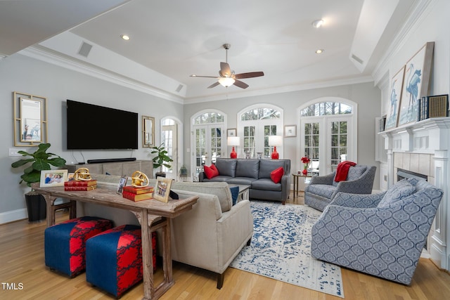 living room featuring a raised ceiling, ceiling fan, a fireplace, and light hardwood / wood-style floors