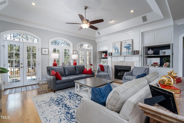 living room featuring french doors, a raised ceiling, a tile fireplace, and built in shelves