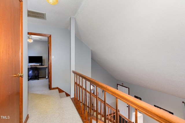 hallway featuring lofted ceiling, light colored carpet, and a textured ceiling