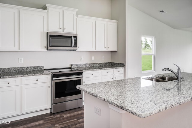 kitchen with white cabinets, appliances with stainless steel finishes, lofted ceiling, sink, and light stone counters