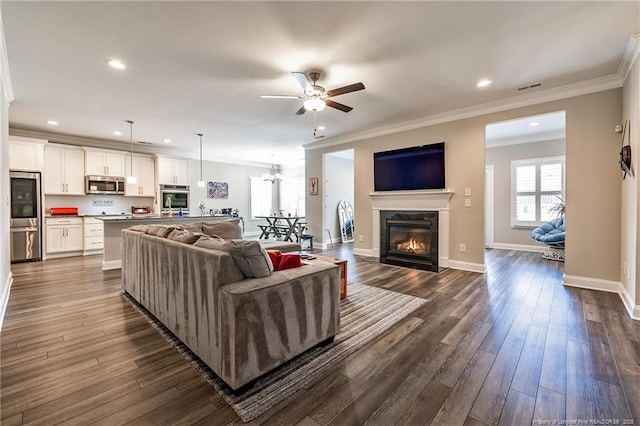 living room with ornamental molding, dark wood-type flooring, and ceiling fan with notable chandelier