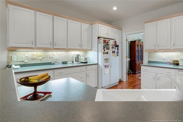 kitchen with white cabinetry, backsplash, white fridge with ice dispenser, and light wood-type flooring