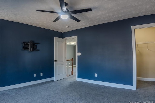 unfurnished bedroom featuring ceiling fan, carpet, a textured ceiling, a spacious closet, and a closet