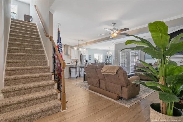 living room featuring ceiling fan with notable chandelier, light hardwood / wood-style flooring, and crown molding