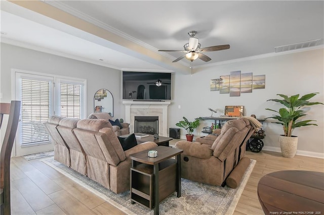 living room featuring ceiling fan, light wood-type flooring, a fireplace, and crown molding