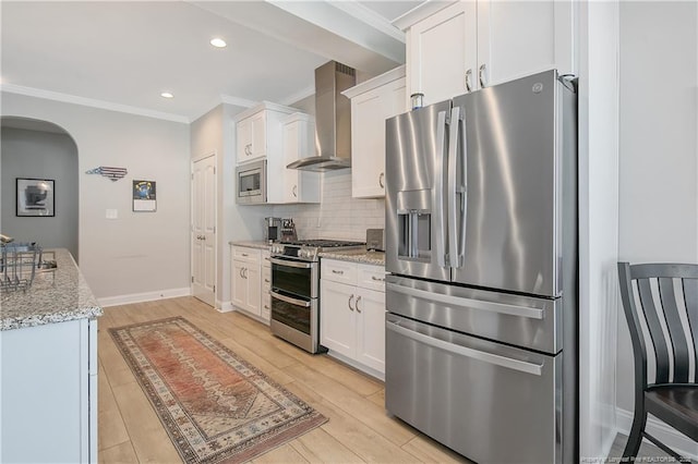 kitchen featuring white cabinetry, light stone counters, wall chimney range hood, and appliances with stainless steel finishes