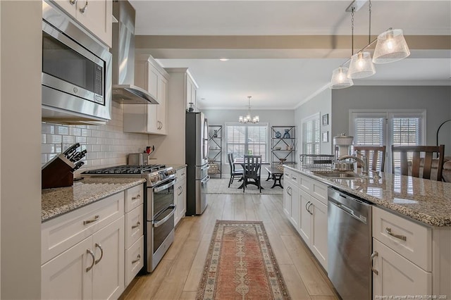 kitchen with white cabinets, appliances with stainless steel finishes, wall chimney exhaust hood, and pendant lighting