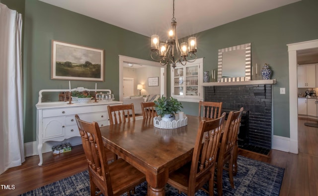 dining area with dark wood-type flooring, a chandelier, and a fireplace