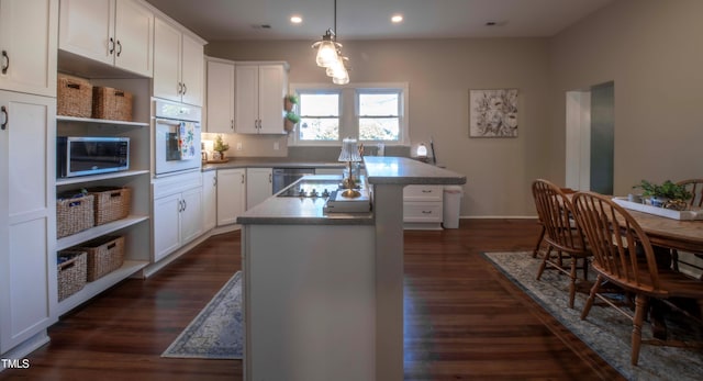 kitchen featuring white oven, dark wood-type flooring, white cabinets, and an island with sink