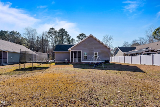 rear view of property featuring a yard, a trampoline, and a sunroom