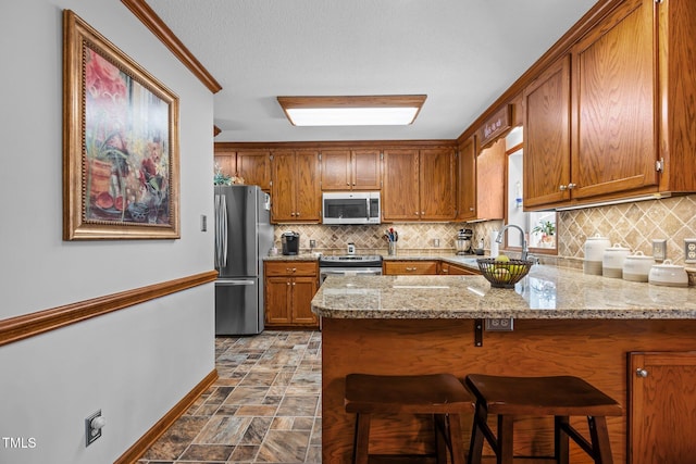 kitchen featuring kitchen peninsula, appliances with stainless steel finishes, light stone counters, and a kitchen bar