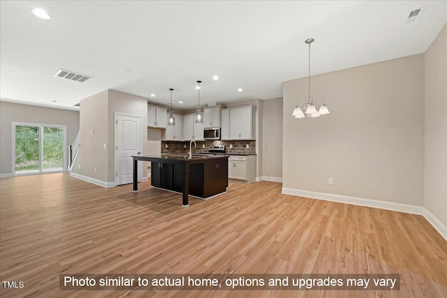 kitchen with white cabinetry, backsplash, a kitchen island with sink, a chandelier, and light hardwood / wood-style flooring