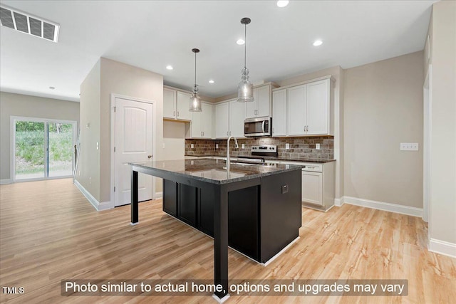 kitchen featuring a kitchen island with sink, white cabinets, dark stone countertops, and appliances with stainless steel finishes