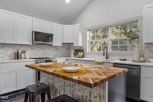 kitchen featuring lofted ceiling, white cabinetry, tasteful backsplash, wooden counters, and stainless steel appliances